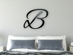 a bed with white sheets and pillows in front of a wall mounted monogrammed clock