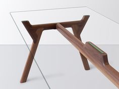 a glass table with wooden legs and a green object in the middle on white background