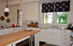 a kitchen with white cabinets and wooden counter tops next to a stove top oven in front of a window