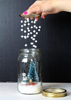 a person is sprinkling snow into a jar with christmas trees in the bottom