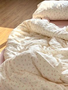 an unmade bed with white sheets and pink flowers on the comforter, in front of a wooden floor