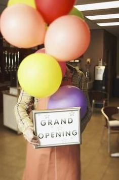 a woman holding a sign that says grand opening with balloons in the air behind her