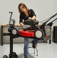 a woman sitting on top of a red lawn mower next to a black table