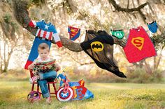 a young boy sitting in a chair under a tree with clothes hanging from the branches