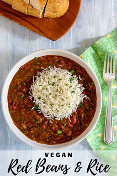 a white bowl filled with chili and rice next to a loaf of bread on top of a wooden cutting board