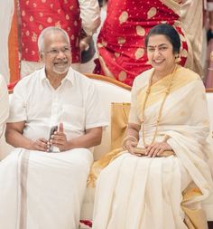 two people sitting next to each other on a white couch with red and gold decorations