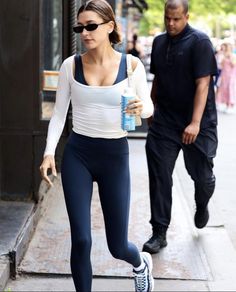 a woman in tights and sneakers walking down the street with a bottle of water