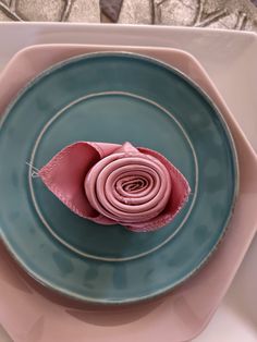 a blue plate with a pink flower on it and a napkin folded in the shape of a rose