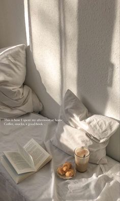 an open book sitting on top of a bed next to a cup of coffee and doughnuts