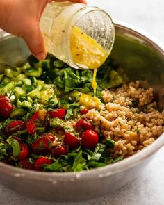 someone pouring dressing into a bowl filled with vegetables and grains, ready to be cooked