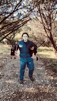 two people in blue jumpsuits and one person wearing a mask standing next to trees