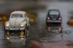 two toy cars sitting on top of a wet surface next to each other in the rain