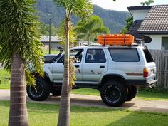 a white suv parked on the side of a road next to a palm tree and house