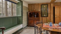 a table and chairs in a room with wood paneling on the walls, along with an old china cabinet