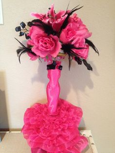 a vase with pink flowers and feathers in it sitting on a table next to a wall