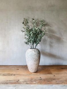 a white vase filled with flowers on top of a wooden table next to a wall