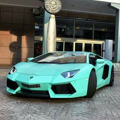 a blue sports car parked in front of a building with a clock on it's side