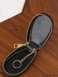 a black leather case with a key chain in it on top of a wooden table