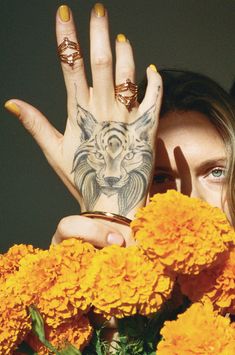 a woman holding her hands up to the camera with yellow flowers in front of her