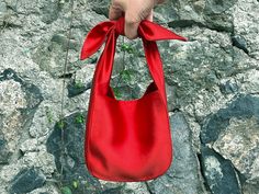 a hand holding a red purse on top of a rock