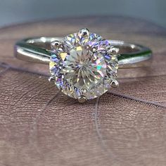 a close up of a diamond ring on a leather surface with a leaf in the foreground