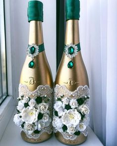 two champagne bottles decorated with white flowers and emerald green ribbon are sitting on a window sill