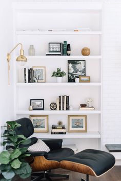 an eames chair and ottoman in front of a bookshelf with pictures on it