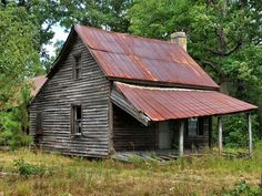 an old wooden house in the woods with rusted tin on it's roof