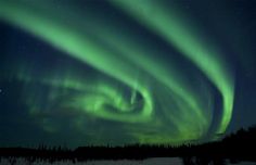 an aurora bore is seen in the night sky over snow covered ground with trees and grass