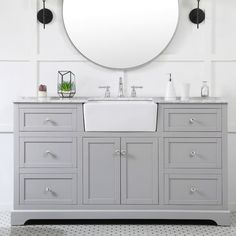 a bathroom vanity with two sinks and a large round mirror above it, in front of a white wall