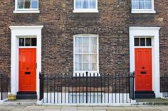 two red doors are in front of a brick building with white windows and black iron fence