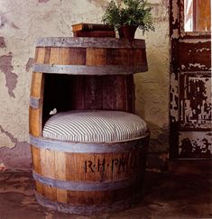 a wooden barrel sitting next to a potted plant on top of a chair in front of a wall