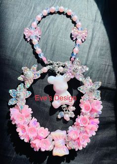 a necklace with pink flowers and a teddy bear charm on the end is attached to a black background