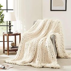 a white knitted blanket sitting on top of a couch next to a table and lamp