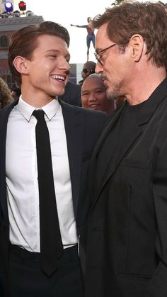 two men standing next to each other in front of a group of people wearing suits and ties