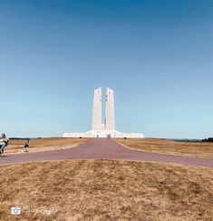 two people walking down a road in front of a tall white monument on top of a hill