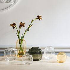 four vases with flowers in them sitting on a table next to a mirror and wall