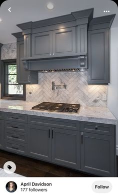 a kitchen with gray cabinets and marble counter tops, along with white tile backsplash