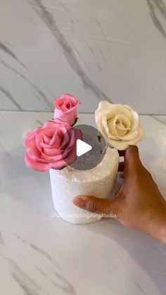 a person is holding some fake flowers in their hand on a white table with marbled surface