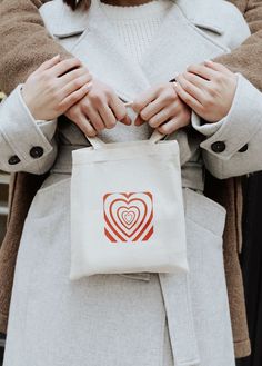 a woman is holding a bag with a heart on it and her hands are in the pocket