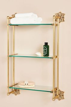 three tiered shelf with glass shelves and gold trimmings on the bottom, along with white towels