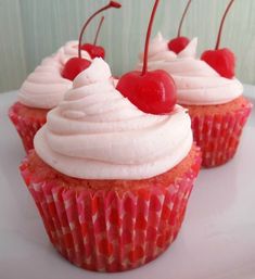 three cupcakes with white frosting and cherries on top are sitting on a plate