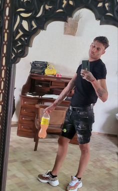 a man standing in front of a mirror holding a cell phone and wearing black shorts