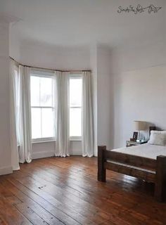 an empty bedroom with wood floors and white curtains on the window sill, next to a bed