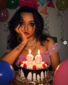 a woman sitting in front of a birthday cake with candles on it and balloons around her