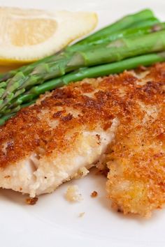 a white plate topped with fish and asparagus next to a lemon wedged slice