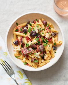 a white bowl filled with pasta, olives and fettuccine on top of a table