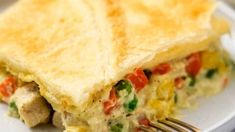 an omelet on a white plate with a fork in the foreground and another food item in the background