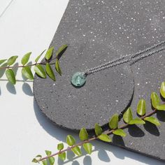 a necklace with a green stone on it sitting on top of a black piece of concrete