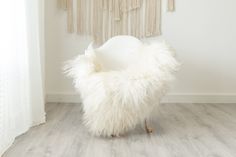 a white chair sitting on top of a hard wood floor next to a wall hanging